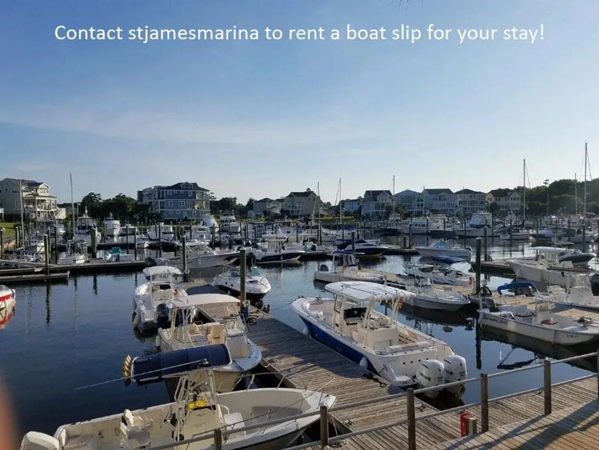A lively marina scene with boats docked along the water, wooden docks stretching out over the reflective surface, and charming waterfront houses in the background. The area conveys a sense of activity and leisure, perfect for boating, fishing, or simply enjoying the atmosphere.