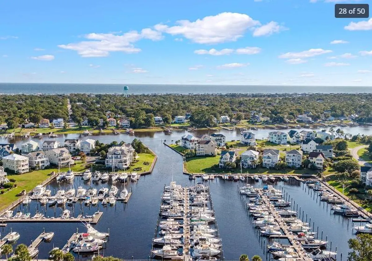 A broad view of the marina featuring boats docked along the waterway, adjacent to a residential area and green spaces. The mood is tranquil, ideal for boating, fishing, or simply taking in the sunset by the water.