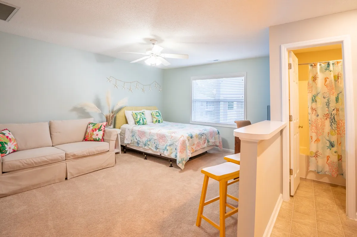 A welcoming room featuring a bed, sofa, decorative elements, a window, and the entrance to a bathroom. The window provides a view to the outside, and the room’s layout suggests opportunities for peaceful mornings or quiet moments of reflection.