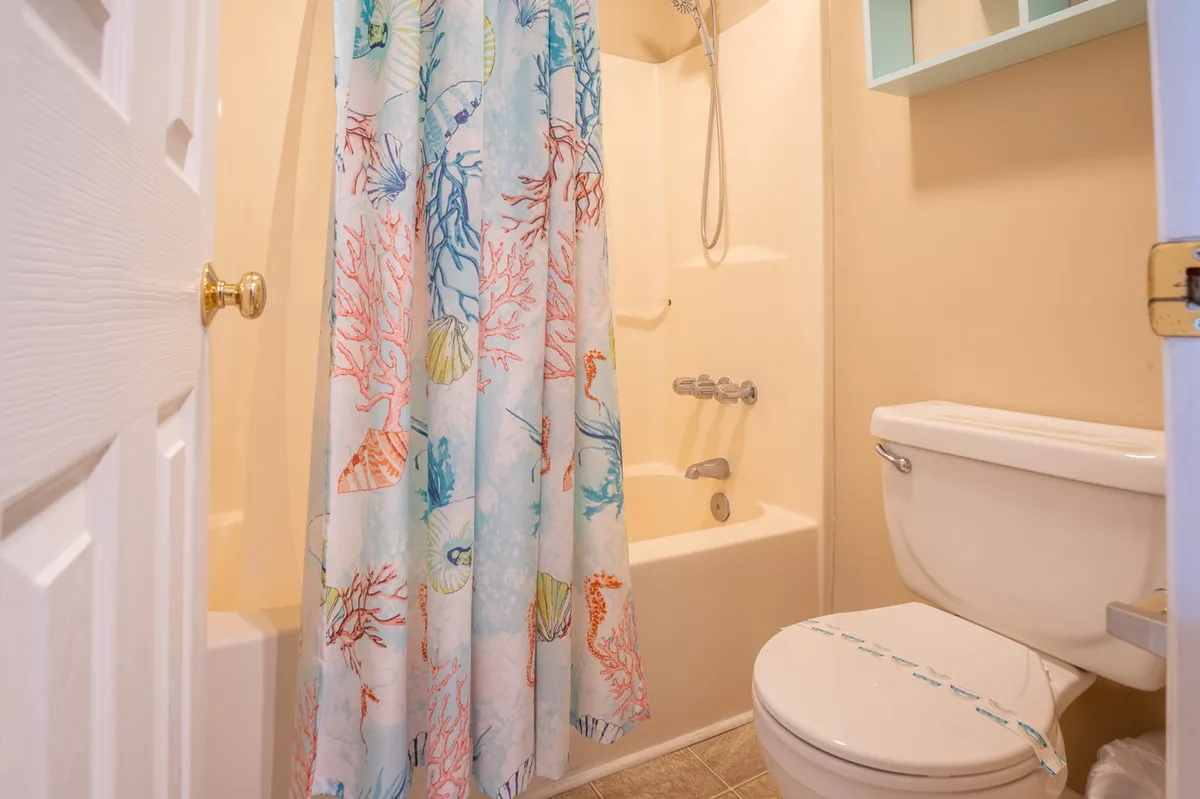 This image highlights a cheerful bathroom with a colorful shower curtain, a well-maintained bathtub, and a toilet, capturing the ensuite bath feature in a welcoming light.