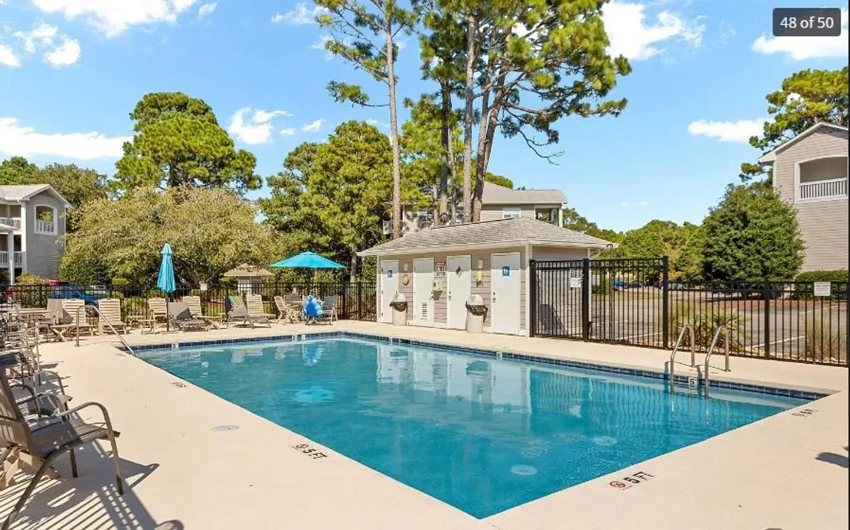 A sparkling outdoor swimming pool surrounded by lounge chairs and umbrellas, set amidst lush greenery. The vibe is leisurely and refreshing, ideal for sunbathing, swimming, and socializing with friends or family.