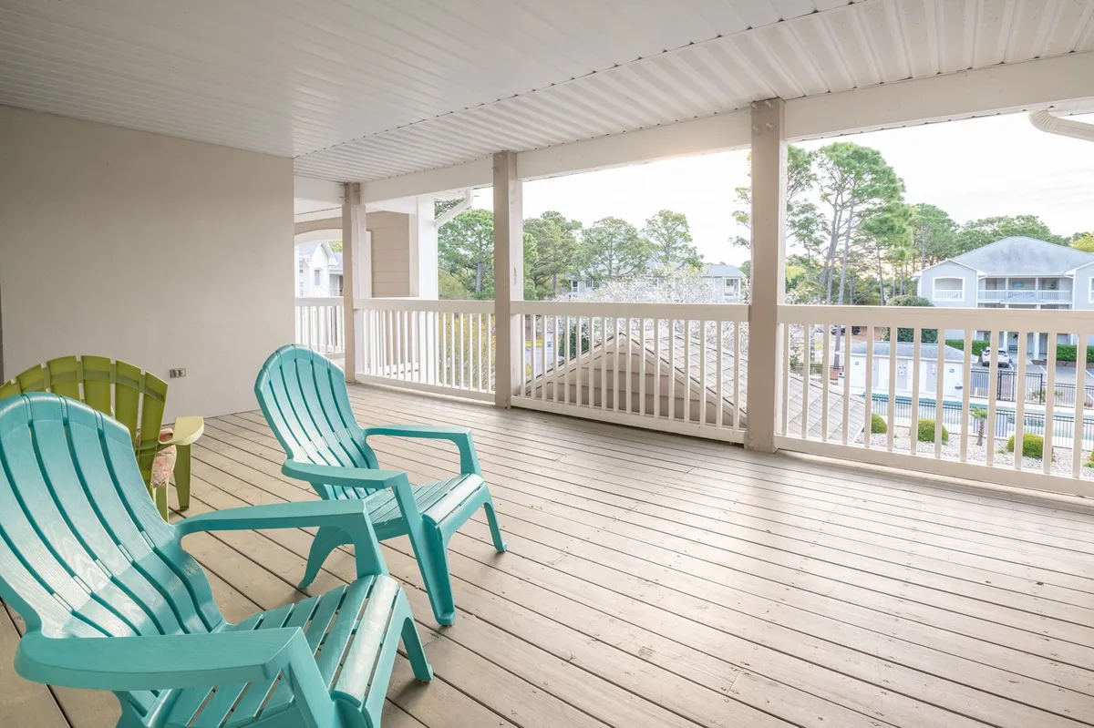 A spacious exterior porch featuring inviting turquoise chairs set on wooden flooring. The porch is surrounded by lush greenery, creating a tranquil environment ideal for relaxing or social gatherings. The scene suggests opportunities for enjoying fresh air, socializing, and unwinding after exploring the resort's amenities.